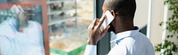 Hombre de negocios afroamericano hablando por teléfono móvil cerca de la ventana, pancarta - foto de stock
