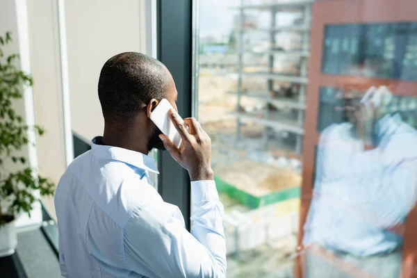 African american businessman calling on cellphone near window in office — Stock Photo