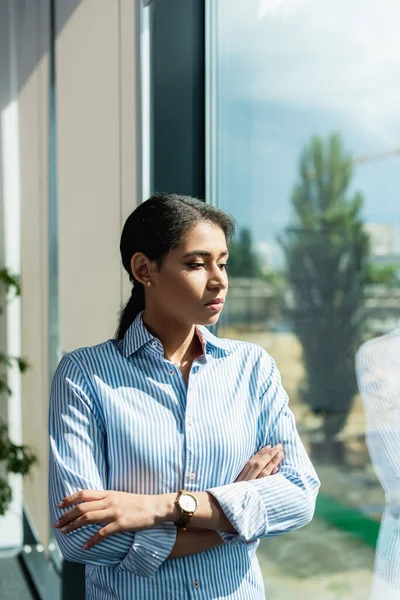 Jovem mulher de negócios afro-americana de pé com braços cruzados enquanto pensa no escritório — Fotografia de Stock
