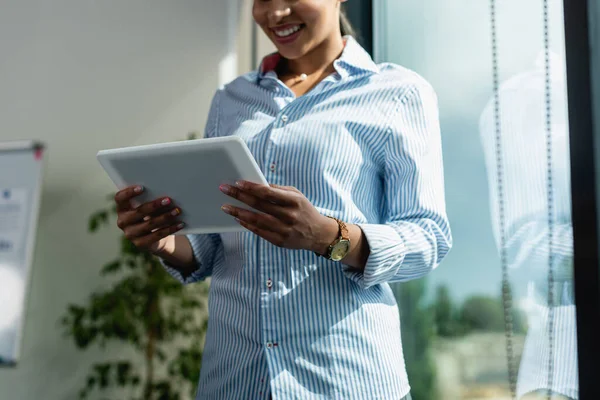 Обрезанный вид улыбающейся африканской американской бизнесвумен с цифровым планшетом в офисе — стоковое фото