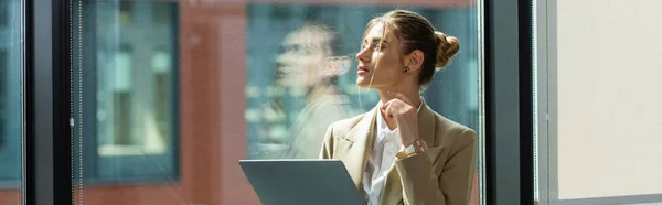 Jeune femme d'affaires avec ordinateur portable penser près de la fenêtre dans le bureau, bannière — Photo de stock