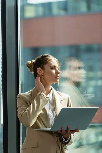 Jeune femme d'affaires avec ordinateur portable penser près de la fenêtre dans le bureau — Photo de stock