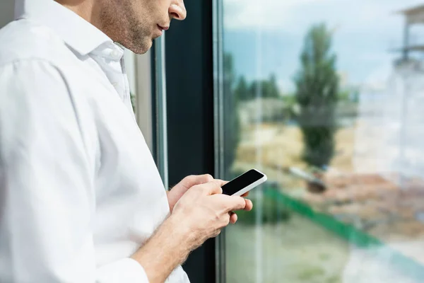 Обрізаний вид обміну повідомленнями бізнесмена на смартфоні біля вікна — стокове фото
