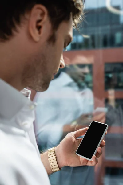 Businessman on blurred foreground holding smartphone with blank screen near window — Stock Photo