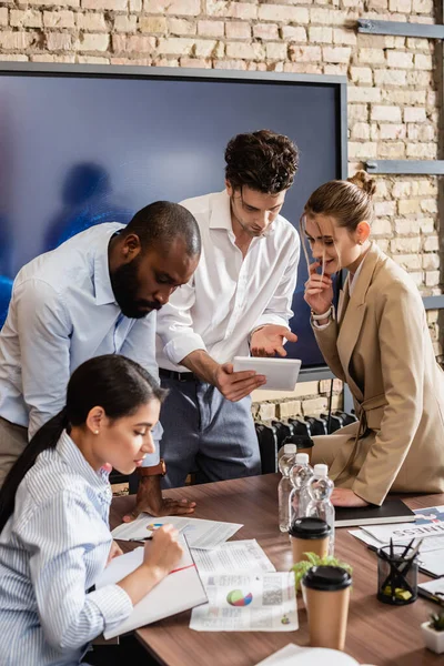 Businessman pointing at digital tablet near interracial business partners in conference room — Stock Photo