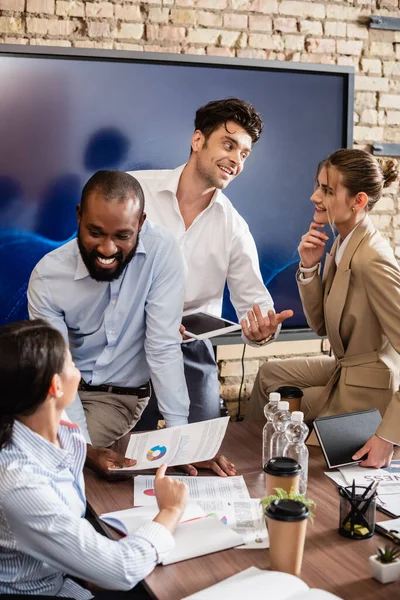 Lächelnde interrassische Geschäftsleute, die sich während einer Besprechung im Konferenzraum unterhalten — Stockfoto