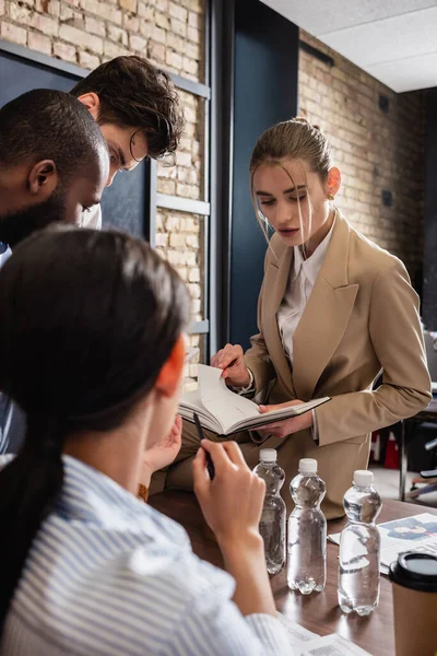 Empresária segurando notebook durante reunião com colegas multiétnicos — Fotografia de Stock