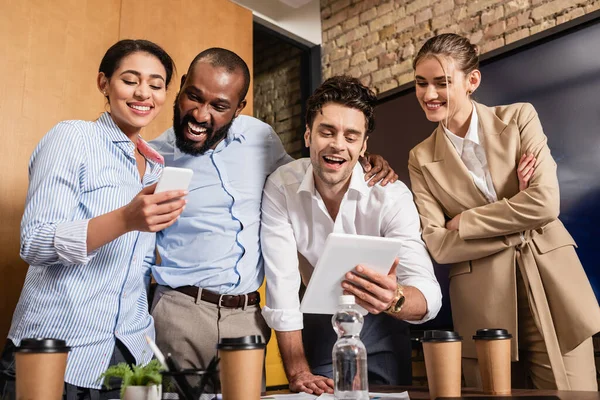 Happy businessman holding digital tablet near excited interracial business partners — Stock Photo
