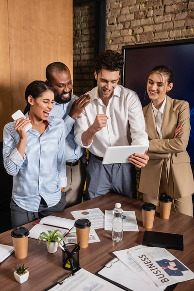 Personas de negocios multiculturales emocionados mostrando gesto de éxito cerca de colega con tableta digital - foto de stock