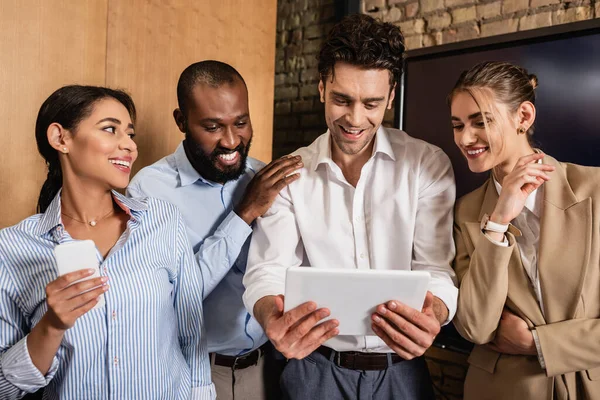 Homme d'affaires heureux regardant tablette numérique près souriant partenaires d'affaires multiethniques — Photo de stock