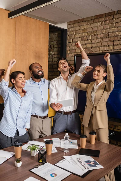 Aufgeregter Geschäftsmann hält digitales Tablet neben fröhlichen Kollegen und zeigt Siegergeste — Stockfoto