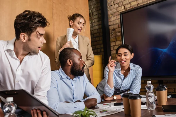 Smiling african american businesswoman showing idea gesture near multiethnic coworkers — Stock Photo