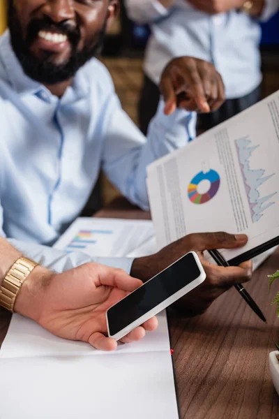 Cropped view of businessman holding smartphone with blank screen near blurred african american colleague — Stock Photo