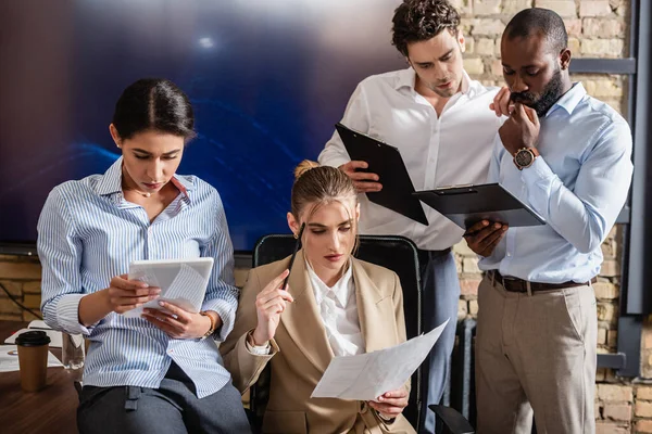 Durchdachte interrassische Geschäftsleute, die im Konferenzraum mit digitalen Tablets und Dokumenten arbeiten — Stockfoto