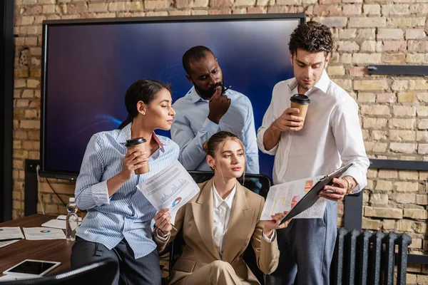 Joven empresario mostrando portapapeles a socios comerciales multiculturales - foto de stock