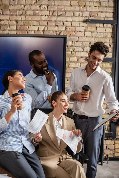 Joyeux interracial hommes d'affaires tenant des documents et du café pour aller dans la salle de réunion — Photo de stock