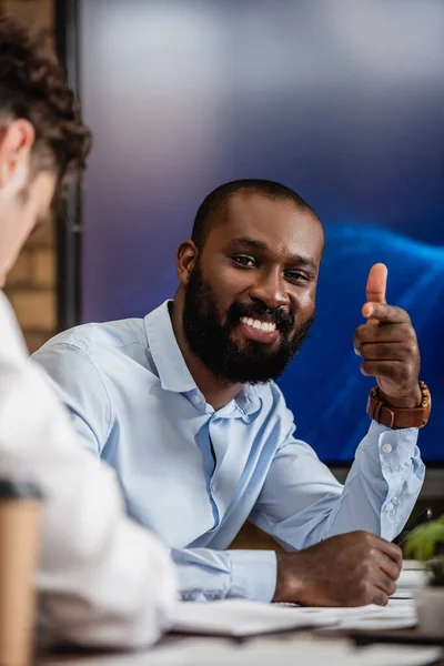 Gioioso uomo d'affari afroamericano che punta con il dito vicino al collega in primo piano sfocato — Foto stock