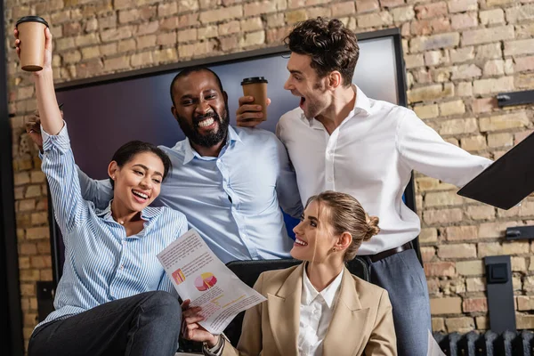 Excited business people with coffee to go and documents talking in conference room — Stock Photo