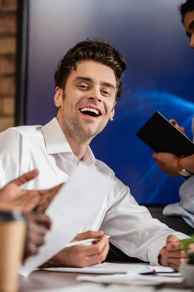 Ridere uomo d'affari guardando la fotocamera vicino sfocato interrazziale colleghi — Foto stock