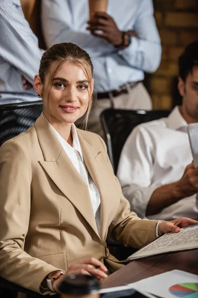 Jeune femme d'affaires souriant à la caméra lors d'une rencontre avec des partenaires d'affaires interracial — Photo de stock