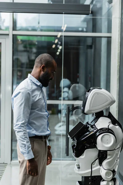 African american engineer looking at humanoid robot in office — Stock Photo