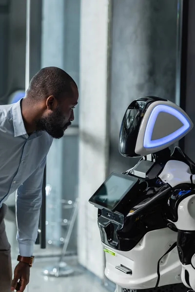 Hombre de negocios afroamericano mirando robot en la oficina - foto de stock