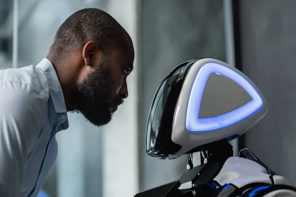 African american engineer looking at humanoid robot in office — Stock Photo