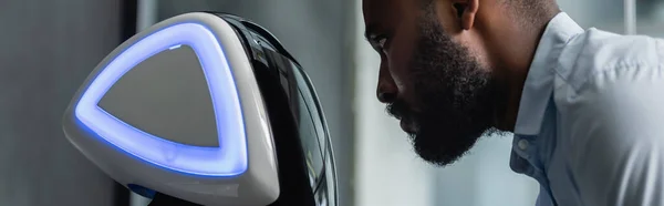 Jeune ingénieur afro-américain près du robot au bureau, bannière — Photo de stock