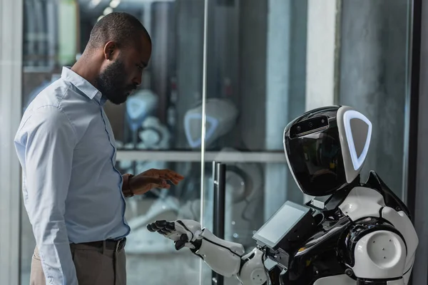 Афроамериканський бізнесмен стоїть біля гуманоїдного робота в офісі — стокове фото