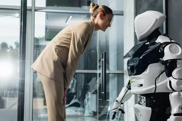 Улыбающаяся деловая женщина смотрит на робота в офисе — стоковое фото