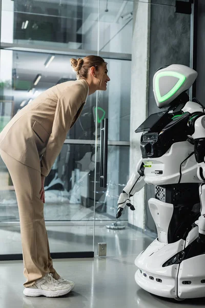 Vista completa de la joven empresaria mirando al robot humanoide en la oficina - foto de stock