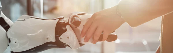 Vista recortada de la mujer de negocios estrechando la mano con robot, pancarta - foto de stock