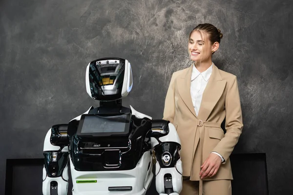 Joyeuse femme d'affaires debout près du robot dans le bureau — Photo de stock