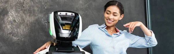 Joyeuse femme d'affaires afro-américaine pointant du doigt le robot au bureau, bannière — Photo de stock