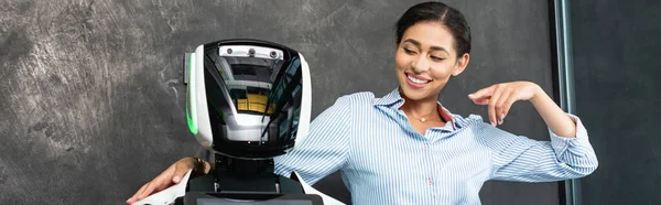 Cheerful african american businesswoman pointing at robot in office, banner — Stock Photo