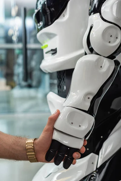 Ausgeschnittene Ansicht eines Ingenieurs, der die Hand eines humanoiden Roboters hält — Stockfoto