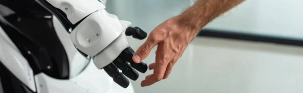 Vue partielle de l'ingénieur touchant la main du robot humanoïde, bannière — Photo de stock