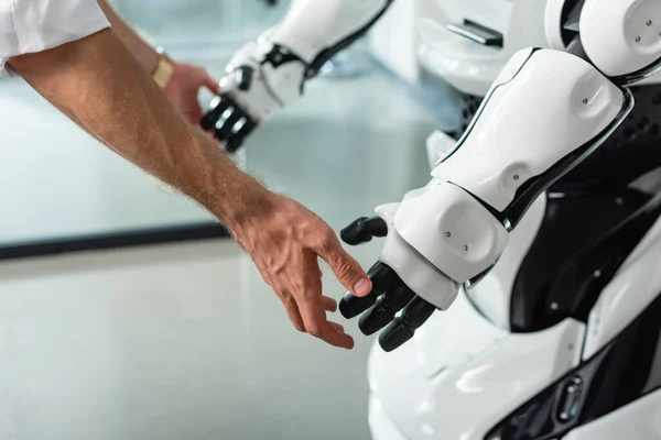 Partial view of engineer touching hands of humanoid robot in office — Stock Photo