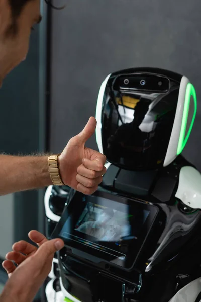 Cropped view of businessman showing thumb up near robot in office — Stock Photo