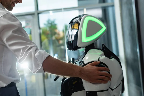 Vista parcial del feliz ingeniero tocando el hombro del robot humanoide en la oficina - foto de stock