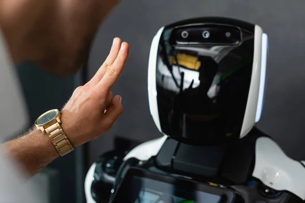 Cropped view of businessman showing victory gesture near robot in office — Stock Photo