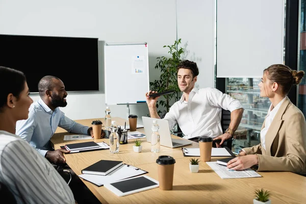 Hombre de negocios feliz celebración de cuaderno durante la reunión con socios comerciales multiétnicos - foto de stock