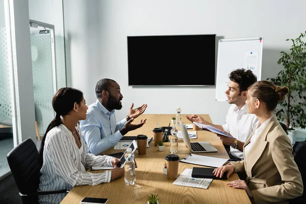 Empresário afro-americano gesticulando enquanto conversa com parceiros de negócios multiétnicos — Fotografia de Stock