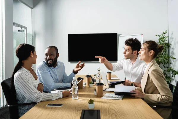 Young businessman pointing with finger near cheerful multicultural colleagues — Stock Photo