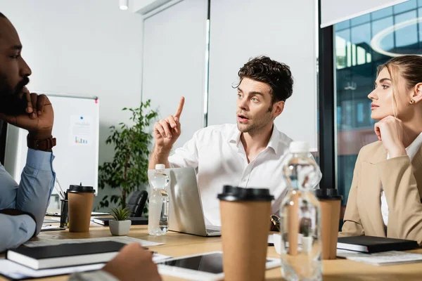 Joven empresario mostrando idea signo durante reunión con colegas interracial - foto de stock