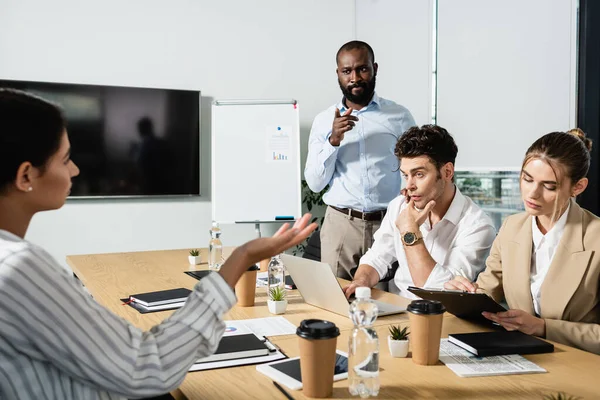 Uomo d'affari afro-americano premuroso che punta il dito durante l'incontro con i colleghi — Foto stock