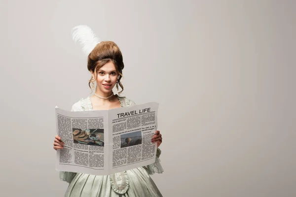 Smiling woman in elegant vintage outfit holding travel life newspaper isolated on grey — Stock Photo