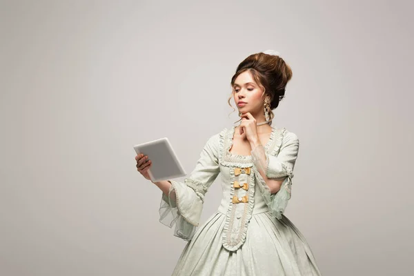 Bella donna in abito vintage pensando mentre guardando tablet digitale isolato su grigio — Foto stock
