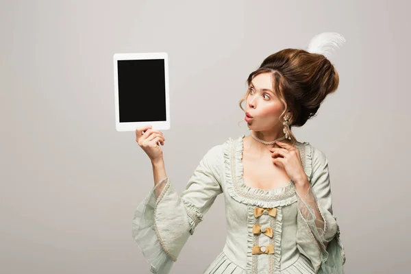 Sorprendida mujer de estilo retro mirando tableta digital con pantalla en blanco aislada en gris - foto de stock