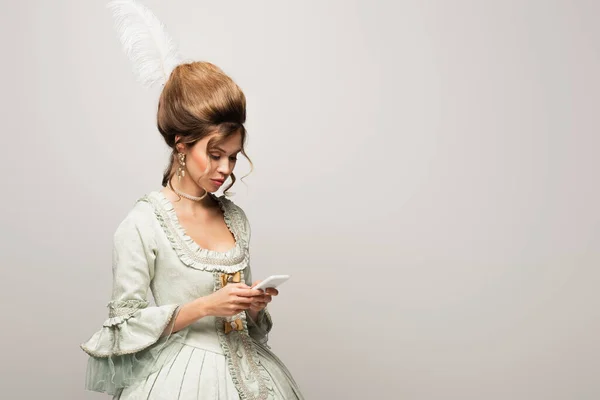 Femme élégante en robe vintage messagerie sur smartphone isolé sur gris — Photo de stock